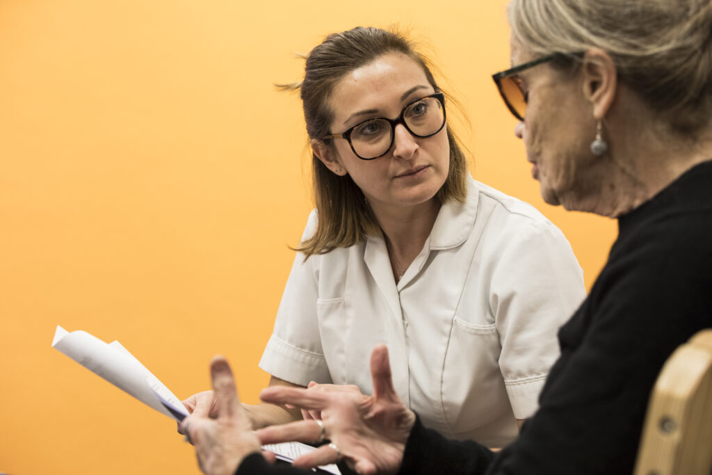 An osteopath is sat down, speaking with a patient about their problems who is talking and gesturing